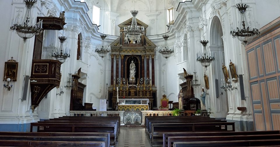 Interno della chiesa di San Cataldo. Pareti bianche decorate con stucchi e altare centrale in legno scuro.
