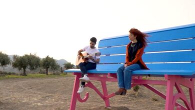 La grande panchina azzurra e fucsia di Centuripe tra gli ulivi, con un ragazzo che suona la chitarra e una ragazza seduta