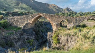 Il Ponte dei Saraceni sul fiume Simeto: ponte medievale in pietra lavica con il grande arco ogivale, tra rocce e colline